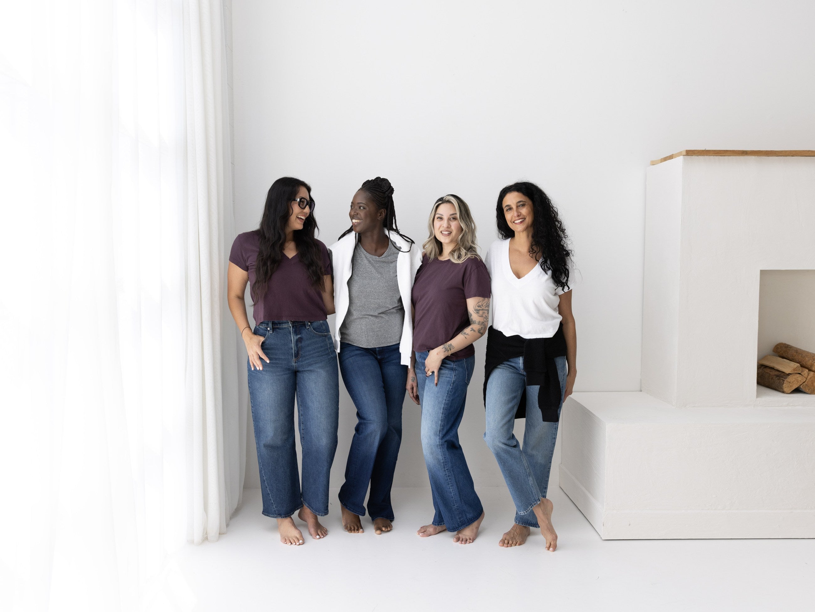 Four friends in everyday tops and denim by a sunlit studio wall
