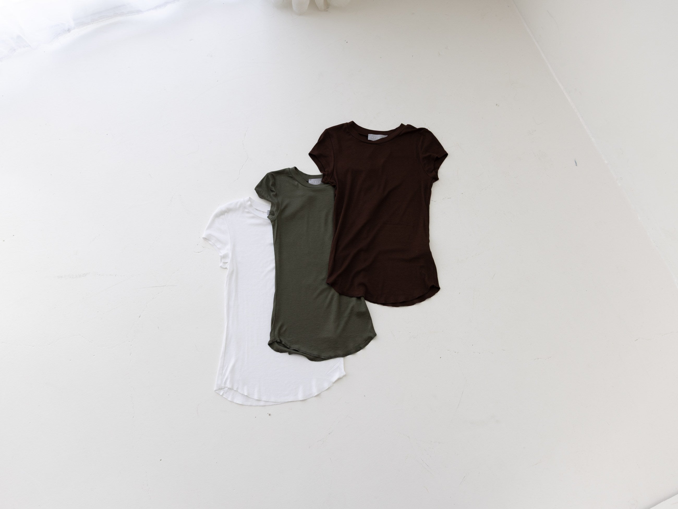 White, olive and brown tops arranged together on a white wall