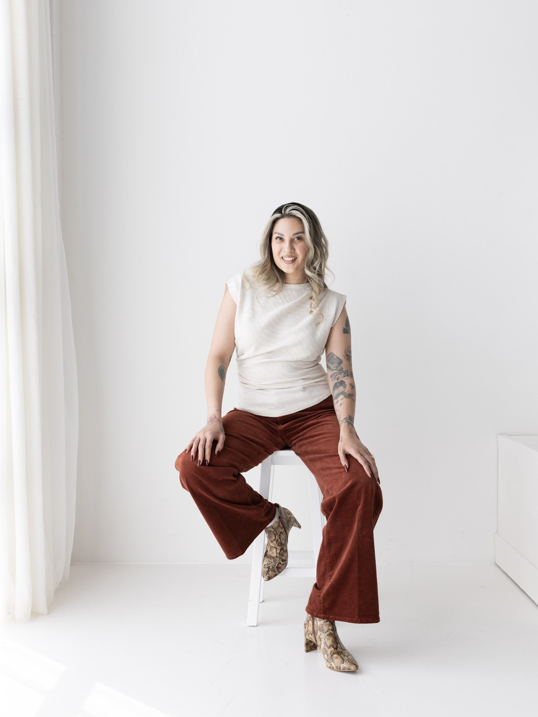 Seated woman in a cream ruched top and rust trousers