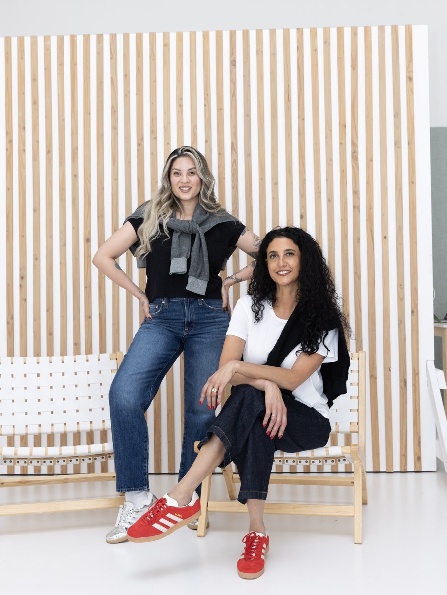 Two women wearing easy layers and denim by the wood slat wall