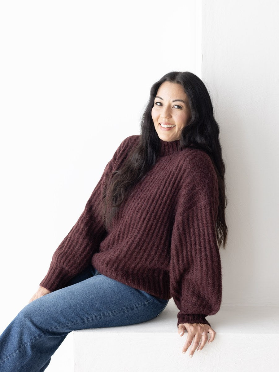 Woman smiling in a burgundy knit and jeans