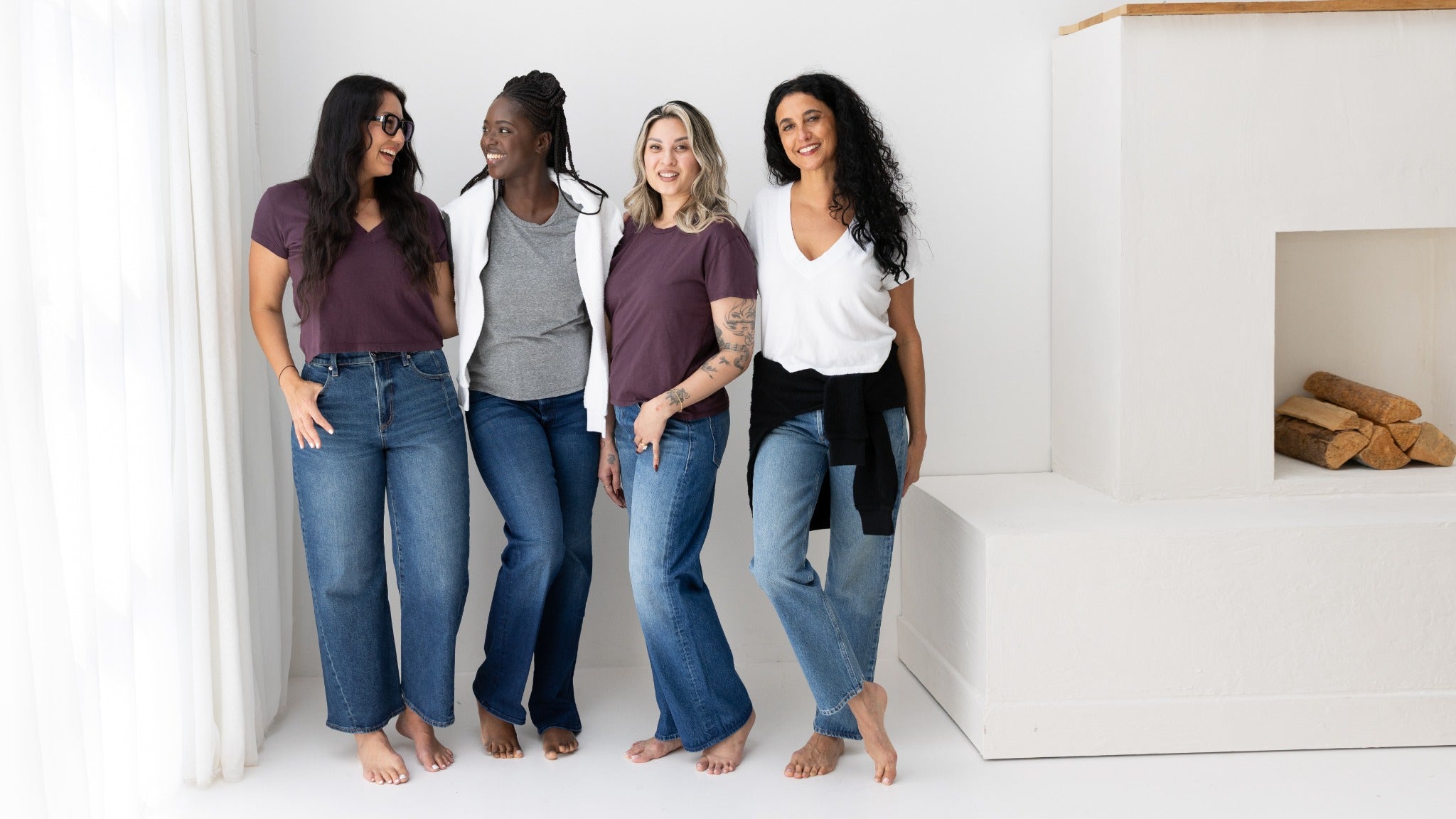 Four women chatting in white tops and denim by the studio fireplace