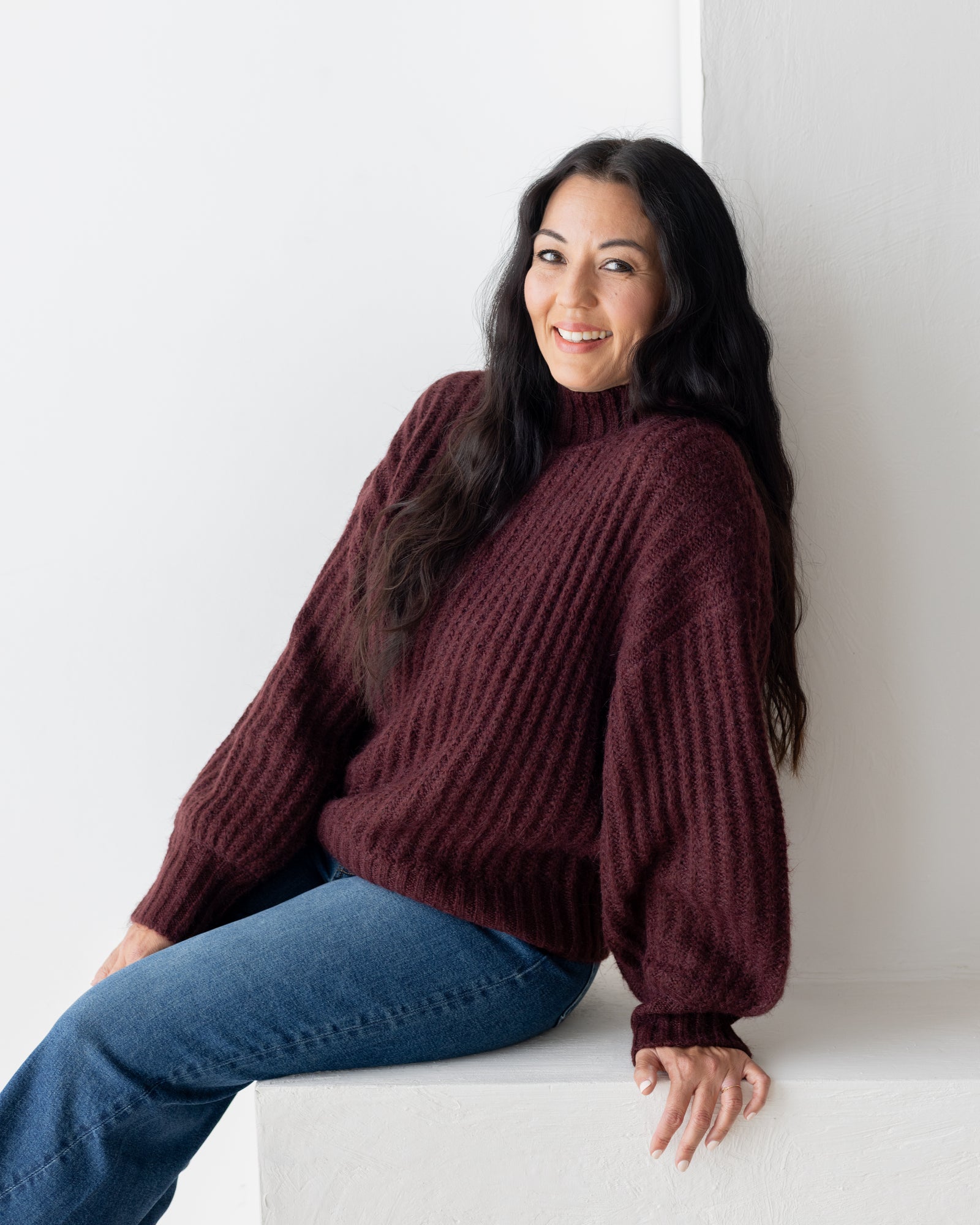 Woman smiling in a burgundy knit and jeans