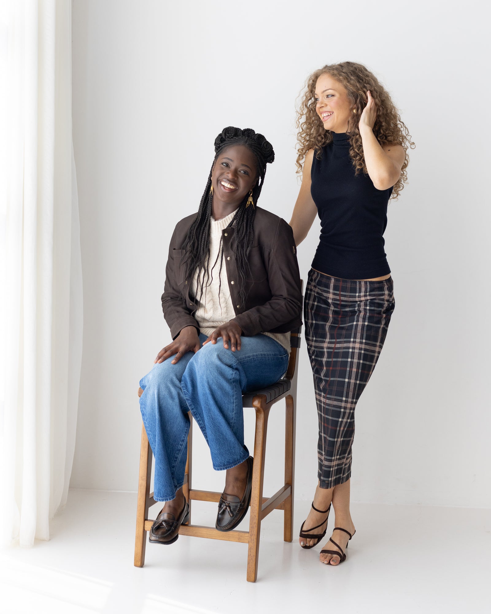 Two women laughing in relaxed denim outfits beside the sofa